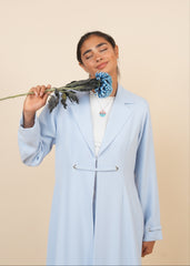 Person wearing a light blue abaya with a floral pattern on a beige background