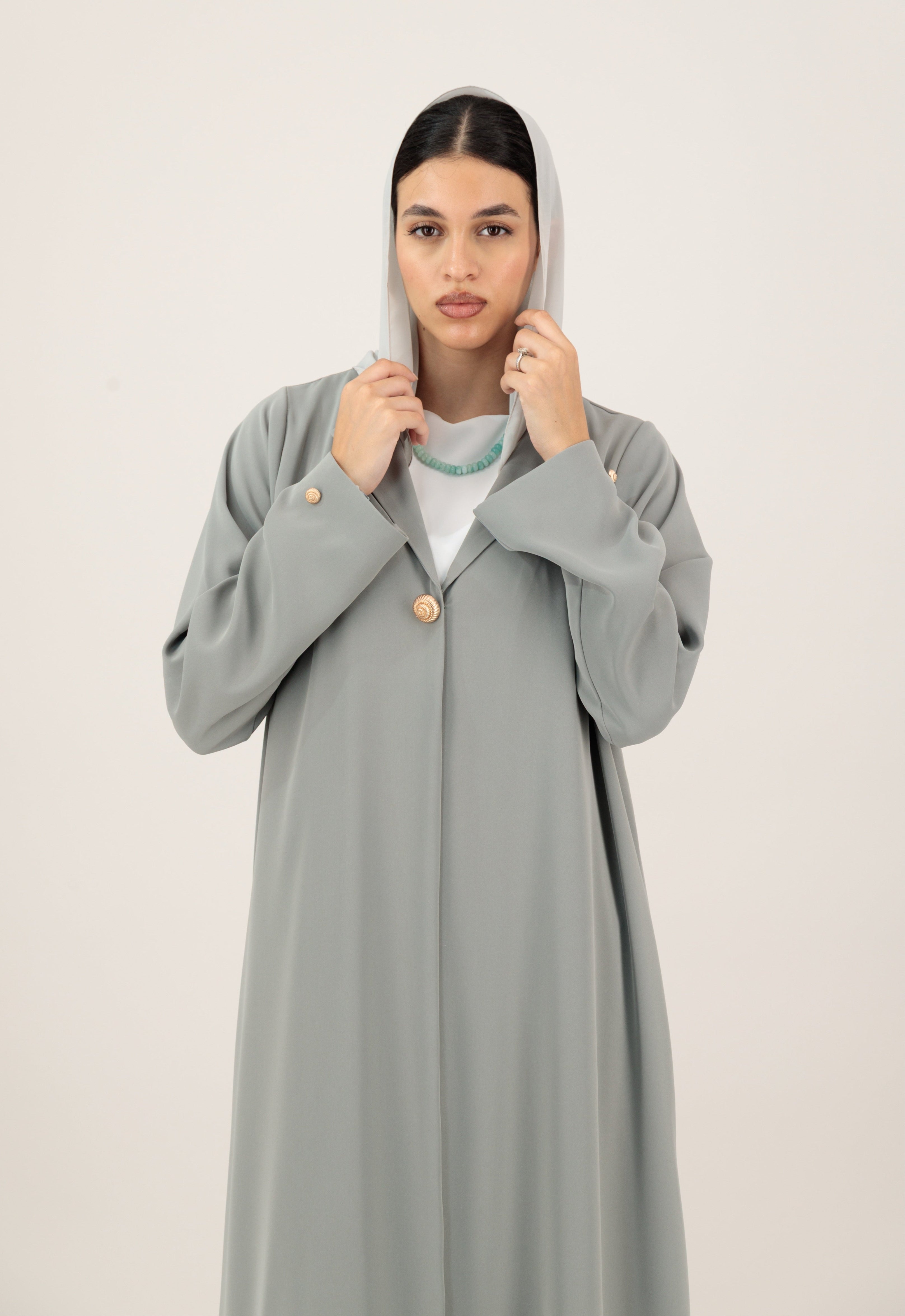 Woman wearing a long gray abaya with a plain background